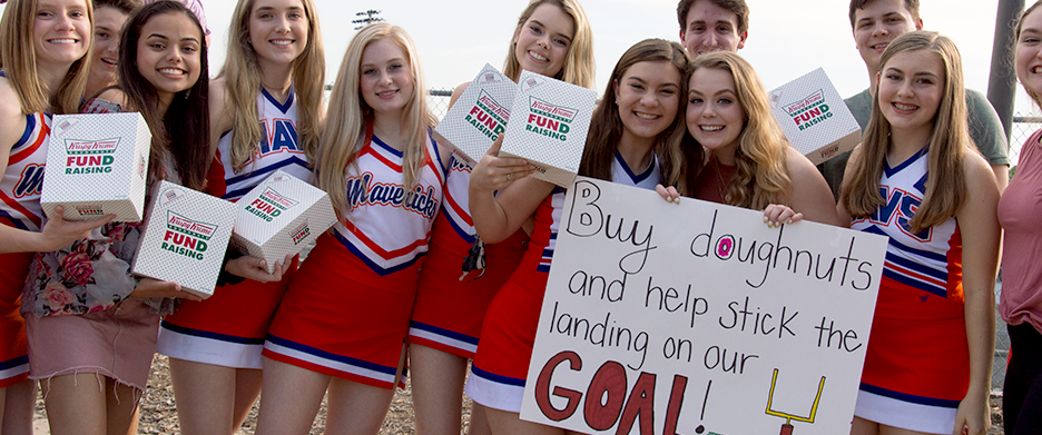 cheerleaders holding a fundraising sign and boxes of doughnuts